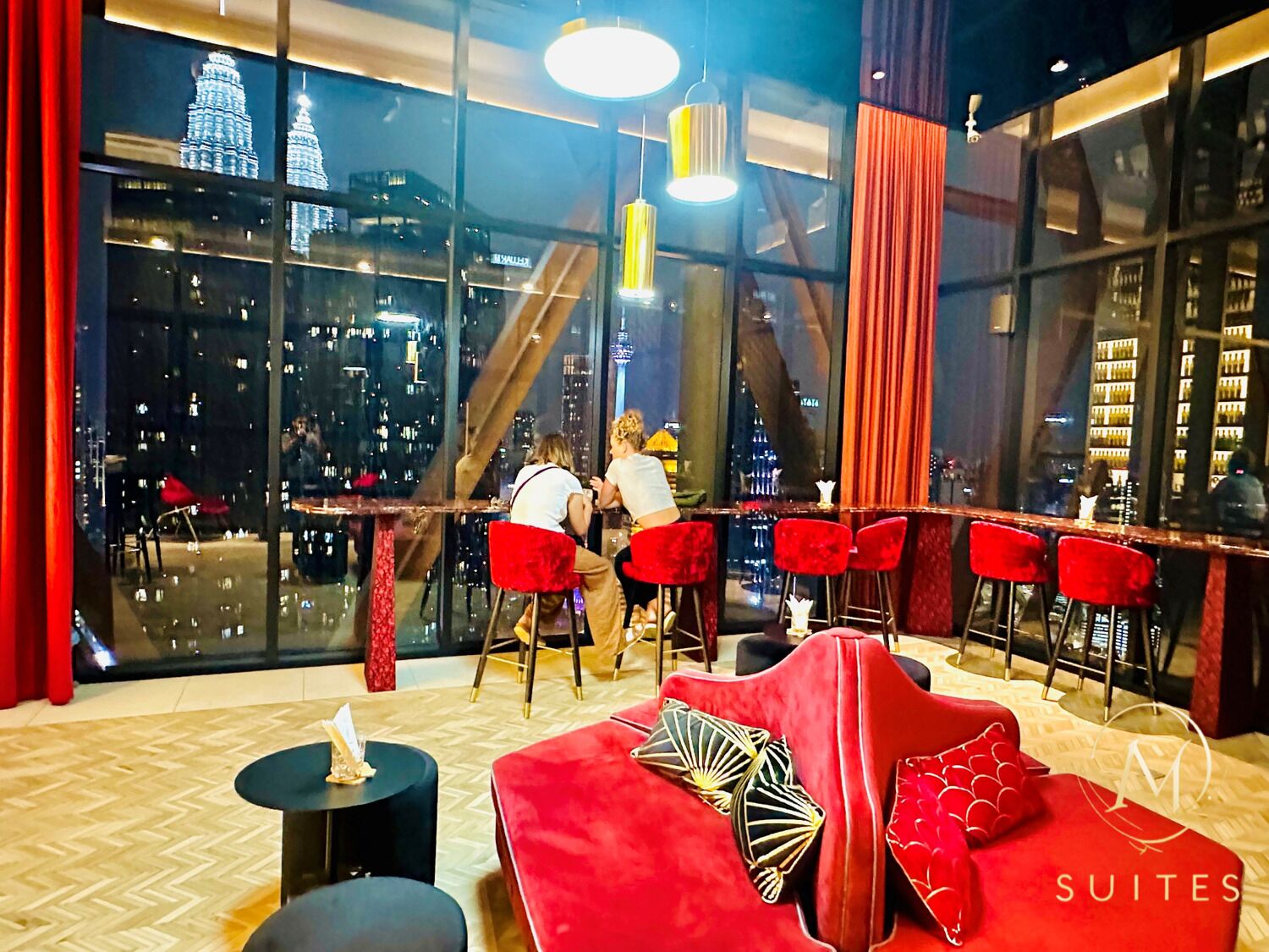 A bar area with red chairs, a red sofa, and a city view through large windows.