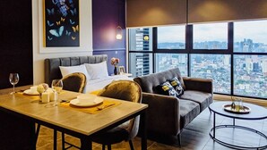 Een moderne woonkamer met uitzicht op de stad, een eethoek met een tafel gedekt voor twee personen, en een groot raam met luxaflex.