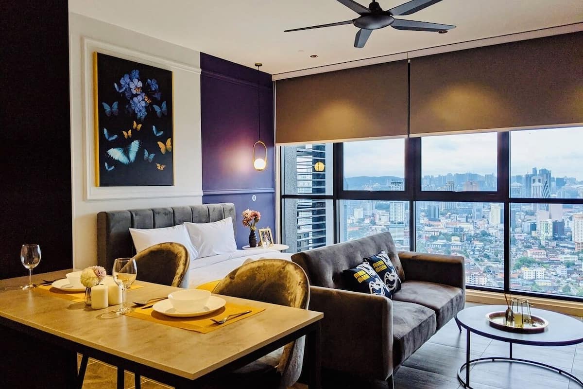 Een moderne woonkamer met uitzicht op de stad, een eethoek met een tafel gedekt voor twee personen, en een groot raam met luxaflex.