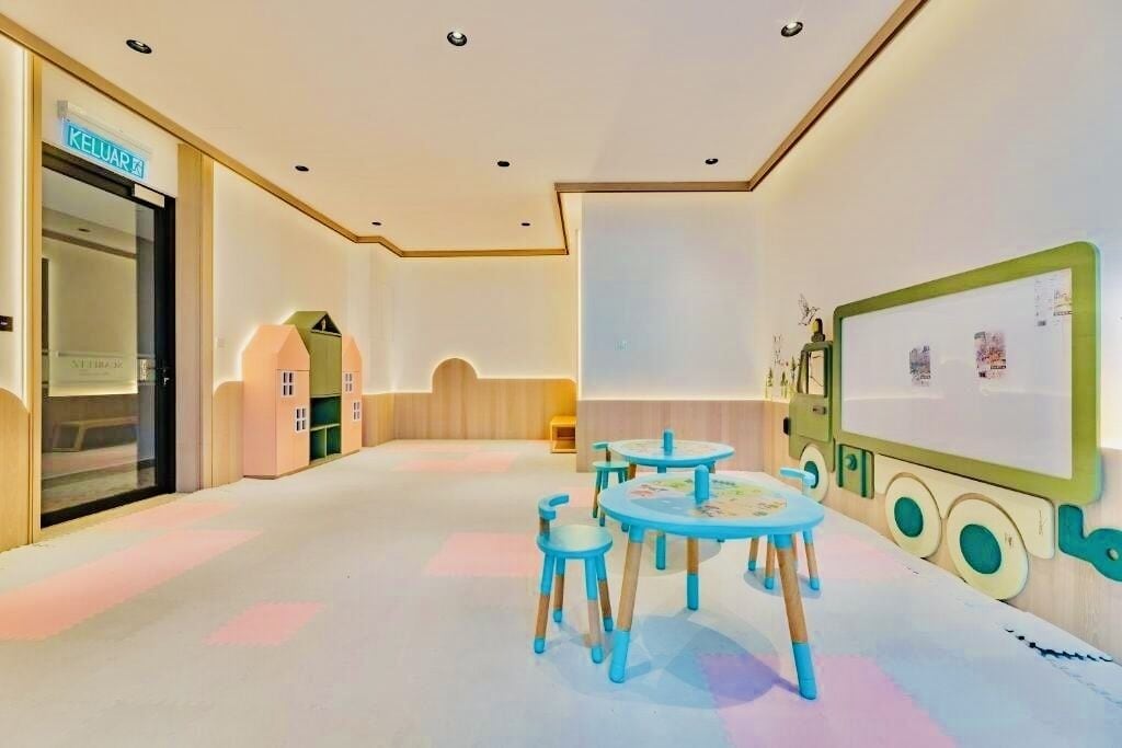 A children's playroom with a table and chairs, a large green screen, and a door labeled "KELUAR".