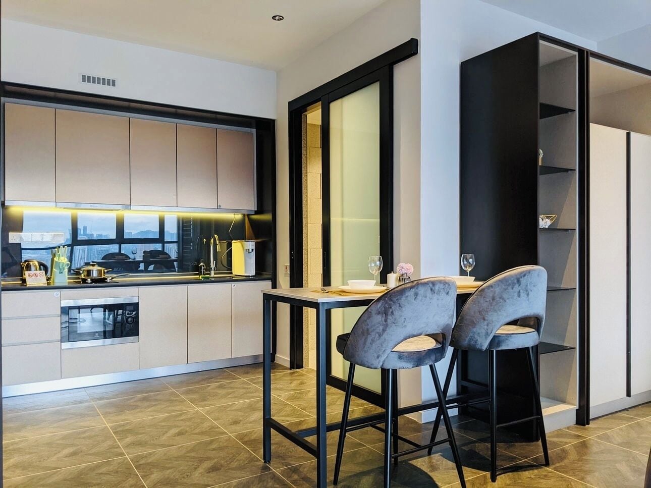 A modern kitchen with a dining area, featuring a built-in oven, a sink, and a dining table with two chairs.
