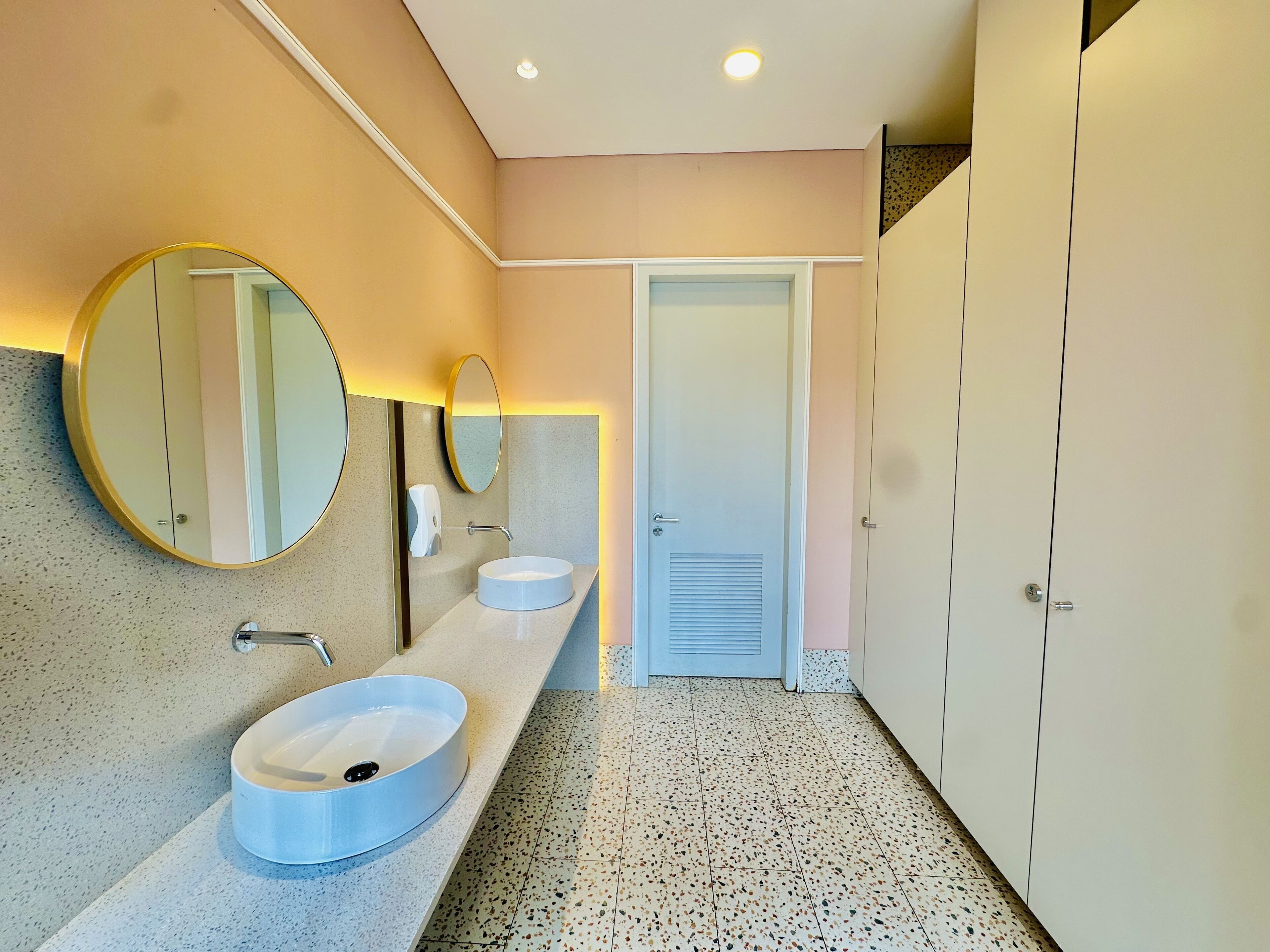 Ein modernes Badezimmer mit zwei Waschbecken, einem großen Spiegel und einer Tür zu einem Abstellraum.