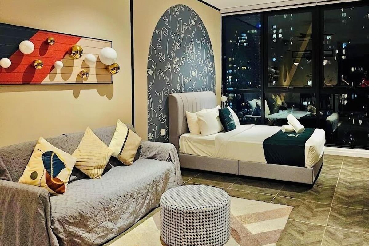 Een moderne woonkamer met een bank, een voetenbankje en een bed met uitzicht op de stad.