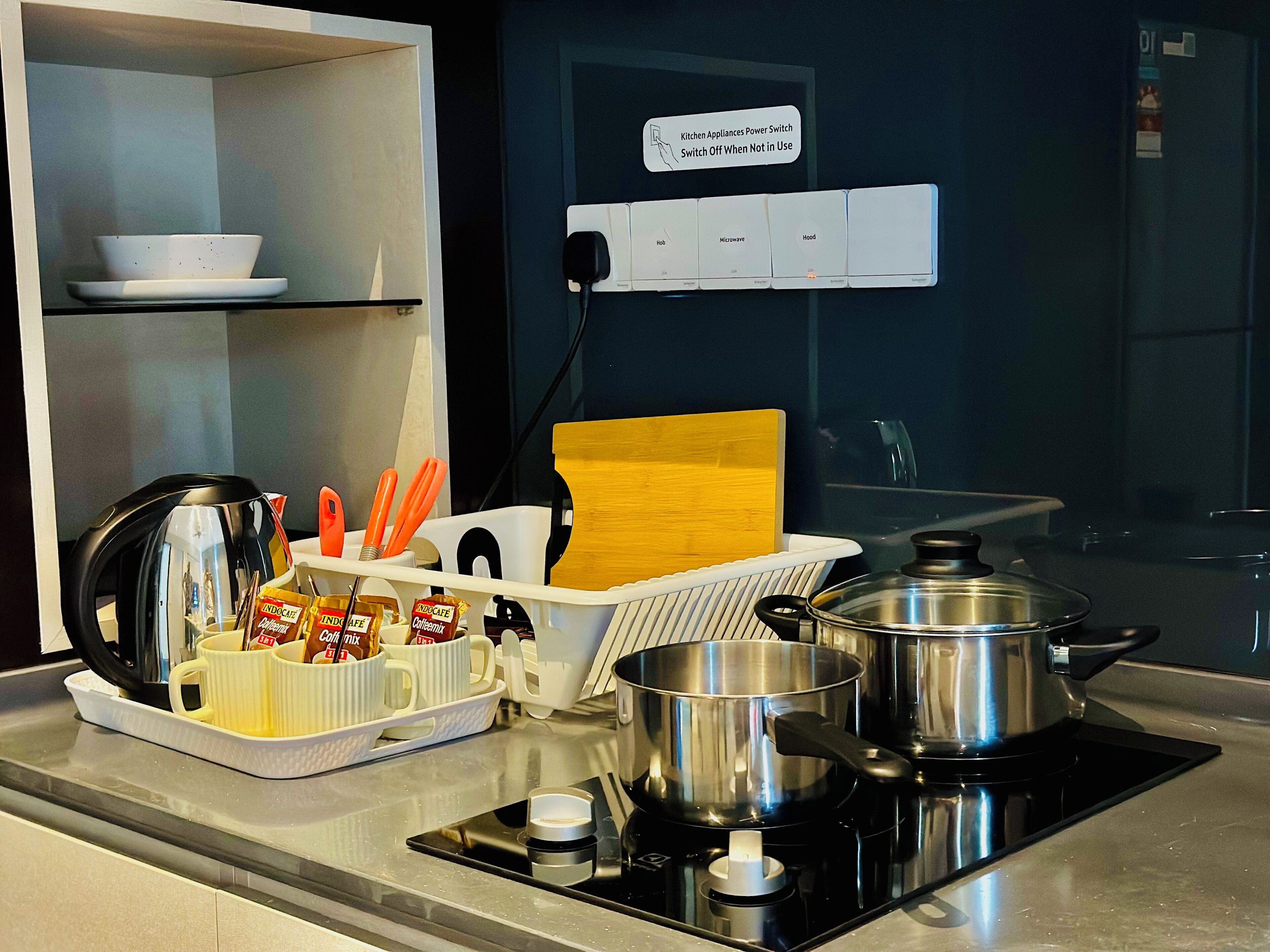 A kitchen with a stove, pots, a coffee maker, and a sign indicating a power switch for kitchen appliances.