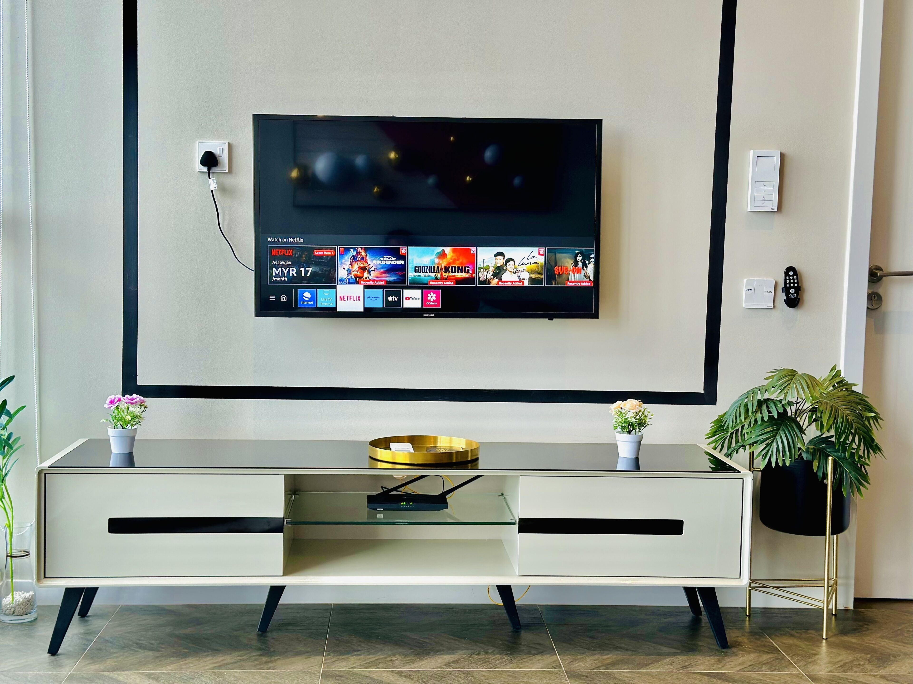 A modern living room with a flat-screen TV mounted on the wall displaying a Netflix interface.