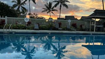 Une piscine bordée de palmiers, avec un coucher de soleil en arrière-plan.