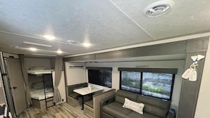 Un intérieur de camping-car compact comprenant un lit superposé, un coin repas, un canapé et un espace cuisine.