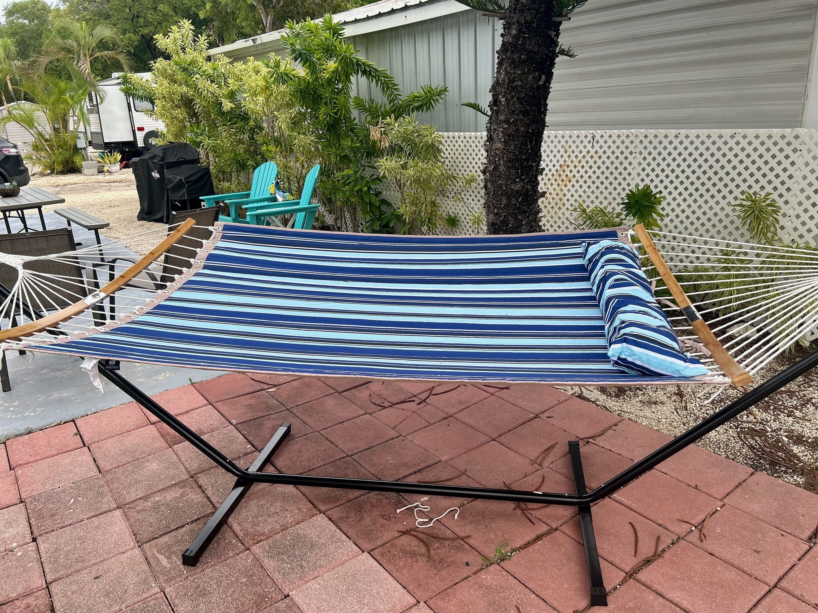 A hammock with a striped fabric, set up on a brick patio with a metal frame.