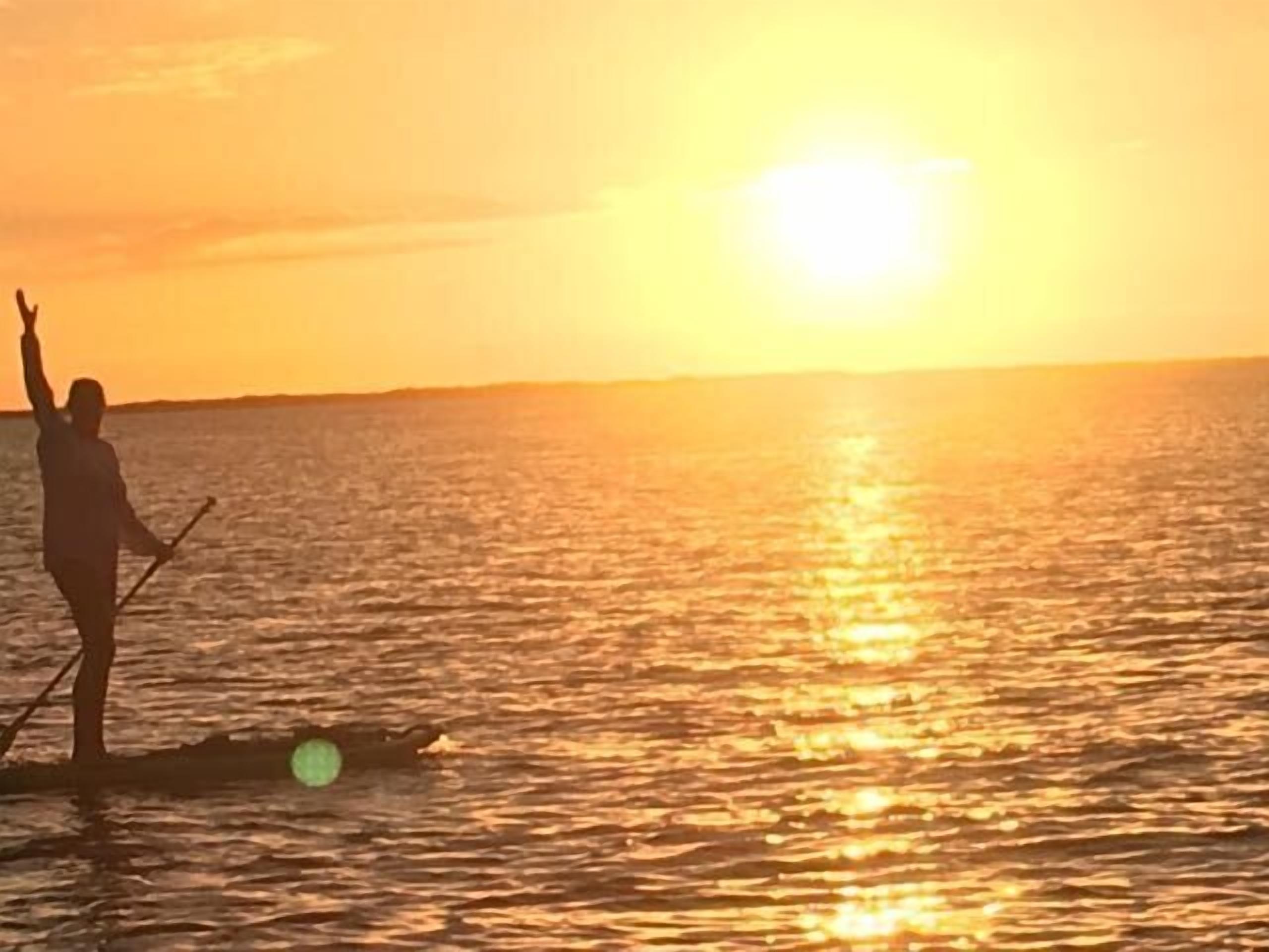 A person standing on a paddleboard in the water during sunset.