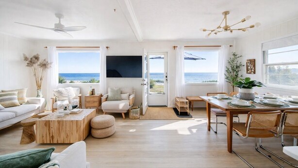 A spacious living room with a large window, a ceiling fan, and a dining area with a view of the sea. - Charming Bungalow on the Bay (East Hampton)