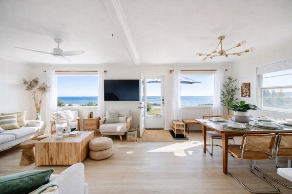 Ein geräumiges Wohnzimmer mit großem Fenster, Deckenventilator und Essbereich mit Meerblick.