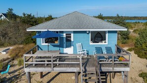 A beach house with a deck, a covered seating area, and a view of the beach and ocean. - Charming Bungalow on the Bay (East Hampton)