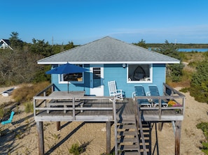 Ein Strandhaus mit Terrasse, überdachter Sitzgelegenheit und Blick auf Strand und Meer.