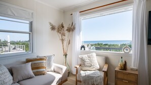 A modern living room with a sofa, armchair, and a small side table with a bottle. - Charming Bungalow on the Bay (East Hampton)