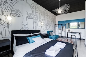 A modern hotel room with a large bed, a desk, and a wall mural.