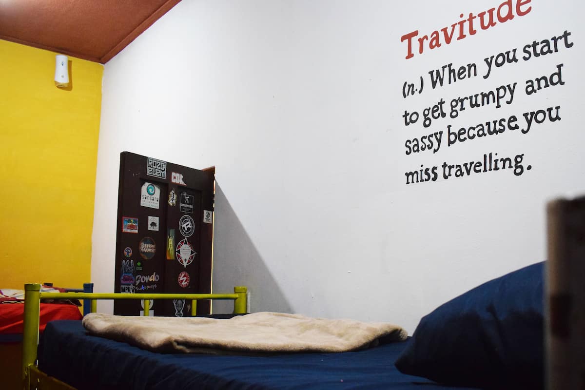 A dorm-style room with a bunk bed, a wall-mounted shelf with various items, and a motivational quote.