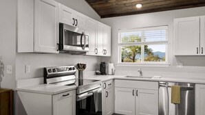 A modern kitchen with white cabinets, stainless steel appliances, and a window with a view of trees and mountains.