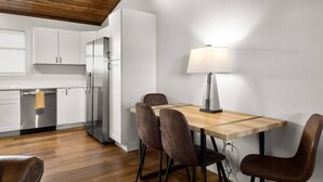 A modern kitchen with white cabinets, a wooden dining table with four chairs, and a hanging light fixture.
