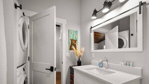A modern bathroom with a white sink, a large mirror, and a washing machine.