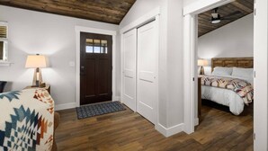 A bedroom with a wooden ceiling, a bed with a patterned blanket, a bedside lamp, and a door leading to another room.