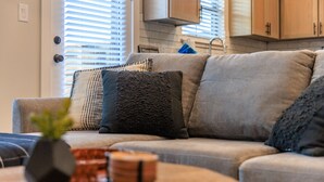 A living room with a grey sofa, multiple cushions, a small plant, and a wooden coffee table. - Brand New Build | Hot Tub | Near Main (Fredericksburg)