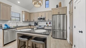 A modern kitchen with wooden cabinets, stainless steel appliances, and a central island with stools. - Brand New Build | Hot Tub | Near Main (Fredericksburg)