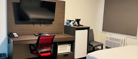 A hotel room with a bed, a desk with a flat-screen TV, a microwave, a coffee maker, and a small refrigerator.