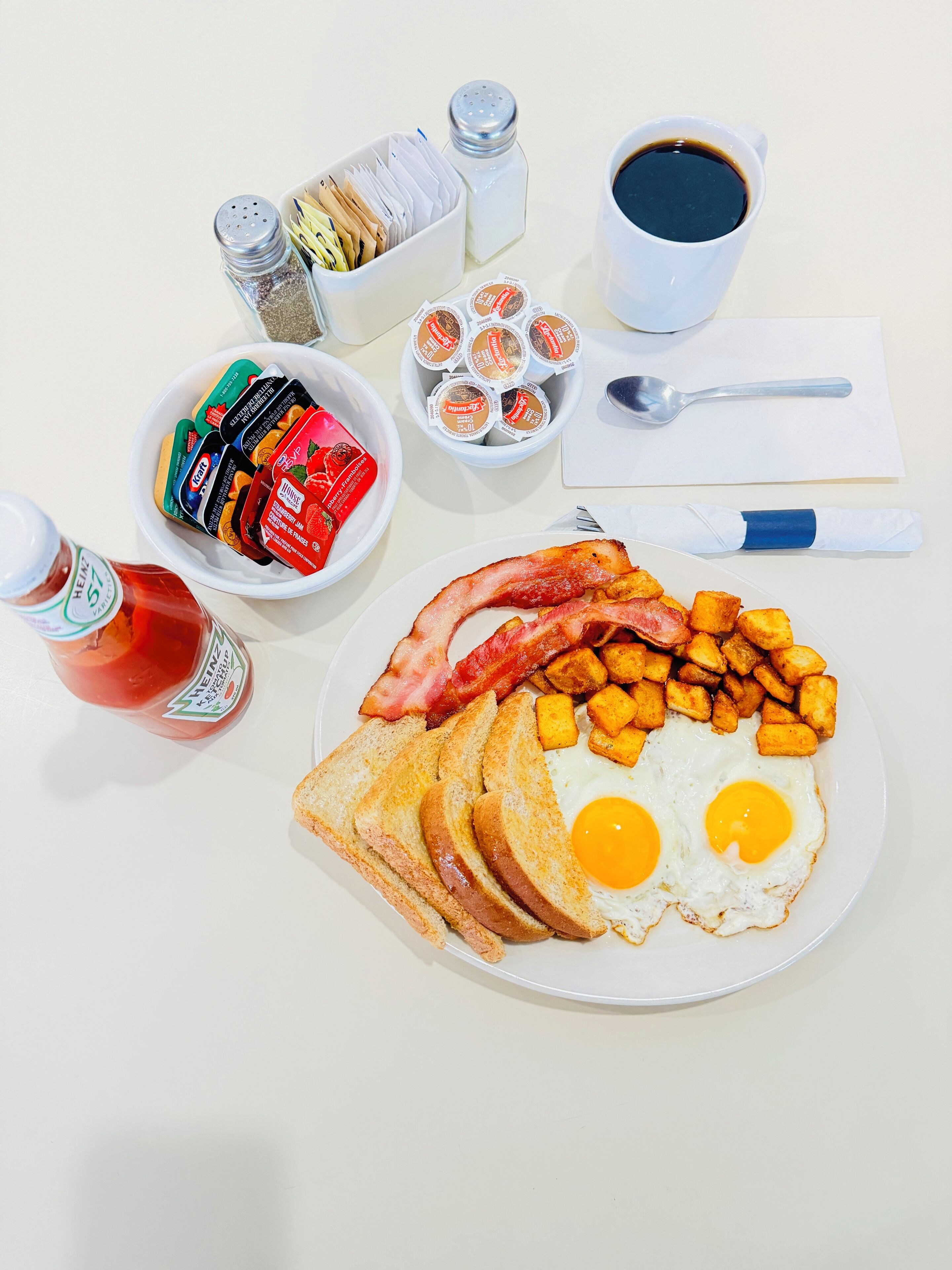 Une assiette de petit-déjeuner comprenant des œufs, du bacon, des toasts et des pommes de terre rissolées.