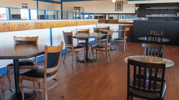 Interior de restaurante con mesas y sillas de madera, una barra con decoración azul y blanca, y una zona de bar.