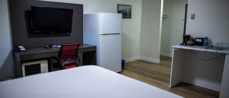 Habitación de hotel con cama, escritorio y silla, televisor, refrigerador y una pequeña zona de kitchenette.