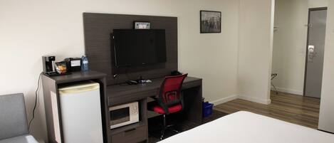 A hotel room with a bed, a desk with a computer, a television, and a microwave.