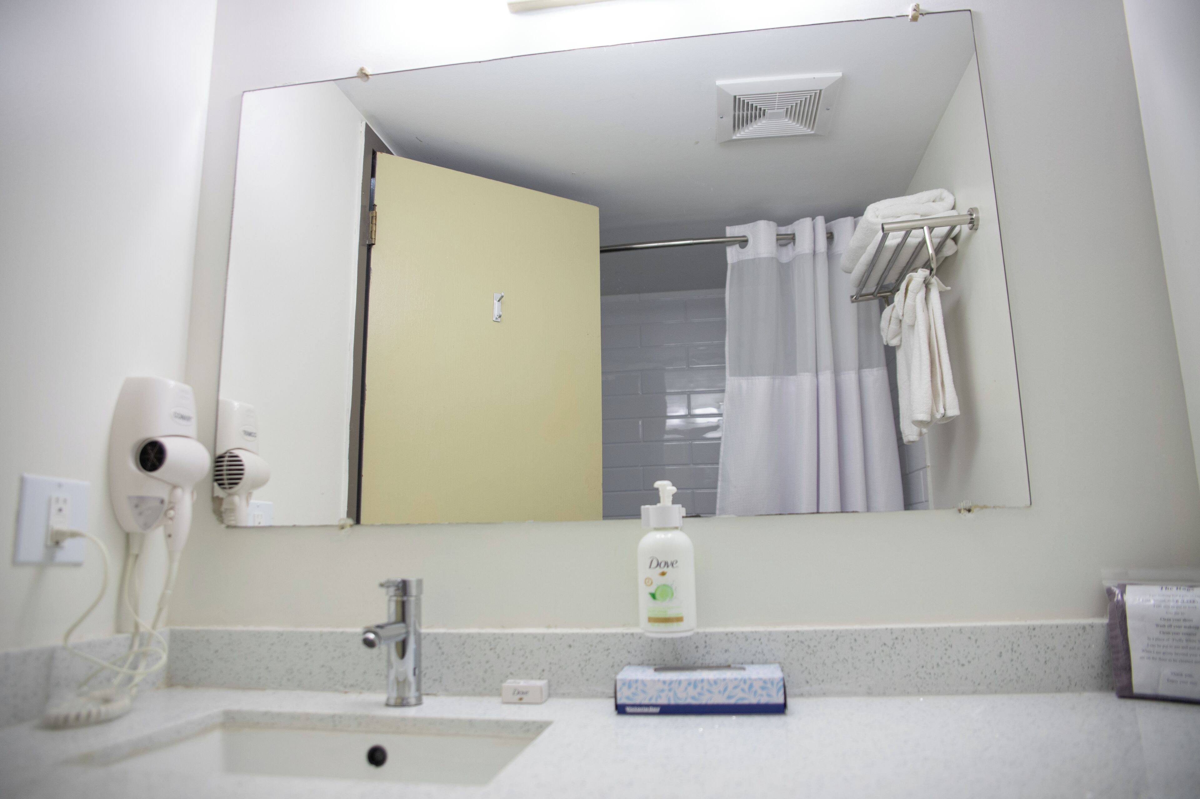 Un baño con lavamanos, espejo, secador de pelo, toallero y una botella de jabón Dove.