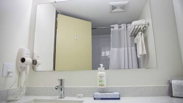 Un baño con lavamanos, espejo, secador de pelo, toallero y una botella de jabón Dove.