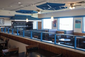 A restaurant with a long counter, blue accents, and a view through large windows. - Ramada by Wyndham Dawson Creek (Dawson Creek)