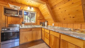 A wooden cabin kitchen with a stove, microwave, sink, and wooden cabinets. - Hot Tub in Beautiful Gazebo, Large Covered Outdoor Dining Area, Playground! (Duck Creek Village)