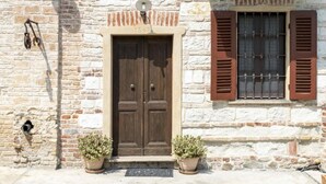 Un bâtiment en pierre doté d’une porte double en bois, d’une petite fenêtre avec volets et de deux plantes en pot placées au sol.