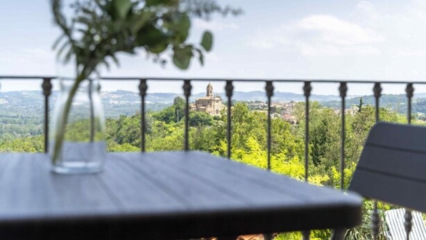 Un balcon offrant une vue sur un bâtiment historique, entouré de verdure.