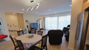 A modern living room with a dining area, a flat-screen TV, and a large window with sheer curtains. - Modern 4BR park-view home in St Johns (Auckland)