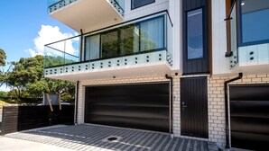A modern two-story house with a balcony, large windows, and a garage. - Modern 4BR park-view home in St Johns (Auckland)