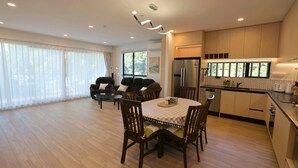 A spacious living area with a dining table, chairs, a sofa, and a kitchen with modern appliances. - Modern 4BR park-view home in St Johns (Auckland)
