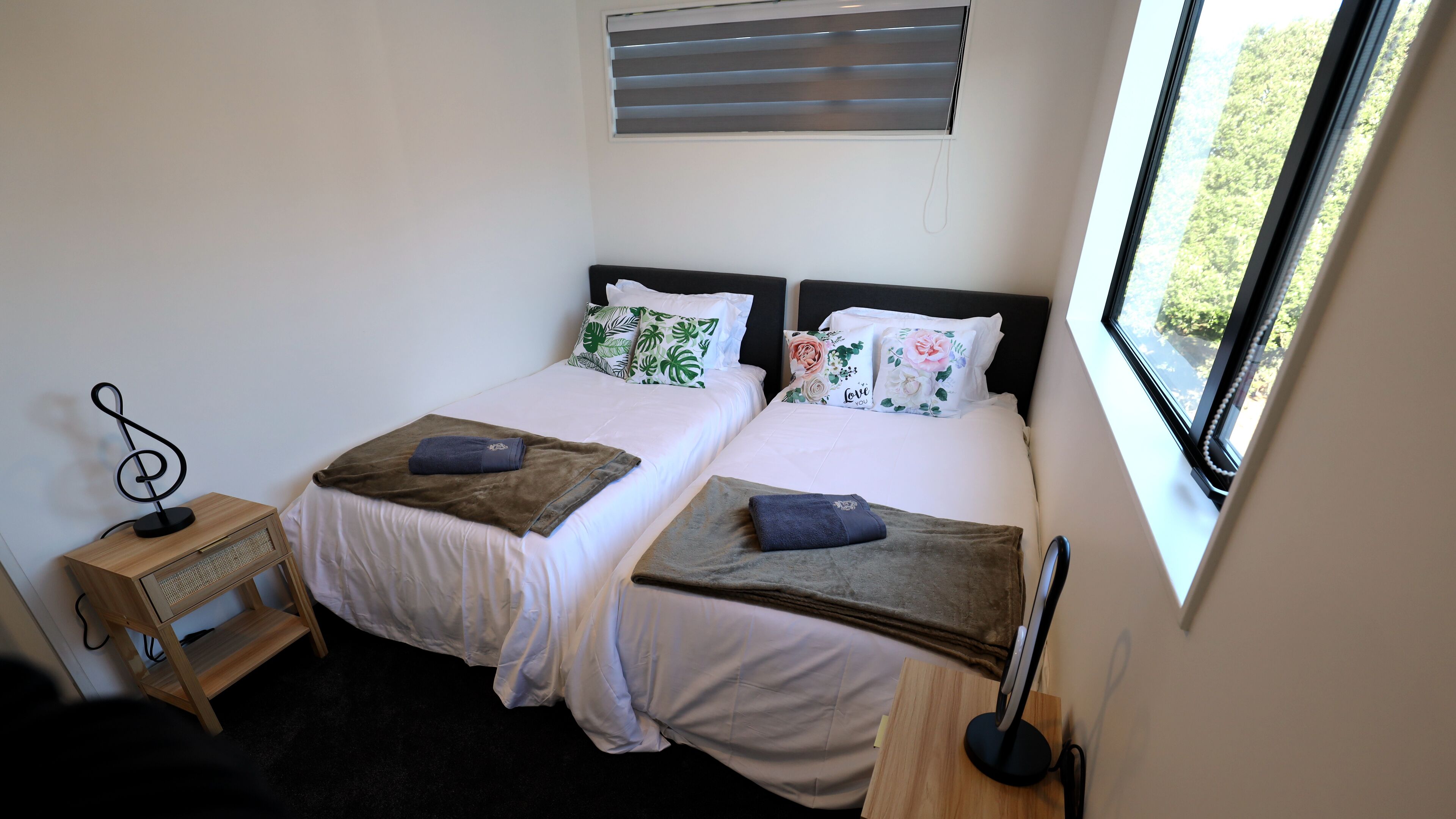 Habitación doble con dos camas, una mesita de noche de madera, un escritorio con ordenador y una ventana con persianas.