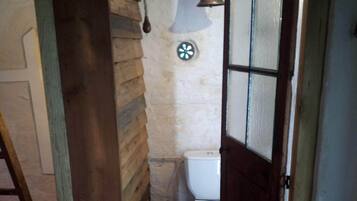 A small, rustic bathroom with a wooden door, a white toilet, and a red floor.