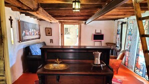 Una habitación rústica con barra de madera, pileta y estufa. Se observa una cruz en la pared y un cuadro enmarcado.