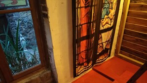Una habitación con alfombra roja, suelo de madera, ventanal con vista a plantas y una puerta de vidrio emplomado.