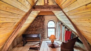 Una habitación cálida en el ático con paredes de madera, una pared de piedra, un banco de madera, una lámpara, un manto de piel y una silla.