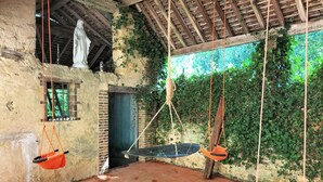 Una habitación rústica con pared de piedra, techo de madera y un columpio suspendido con cuerdas.