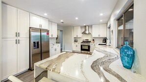 A modern kitchen with white cabinets, a stainless steel refrigerator, a built-in oven, and a marble countertop. - Upscale private paradise on large dog-friendly lot w/ free EV charger (Palm Springs)