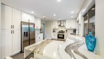 A modern kitchen with white cabinets, a stainless steel refrigerator, a built-in oven, and a marble countertop.