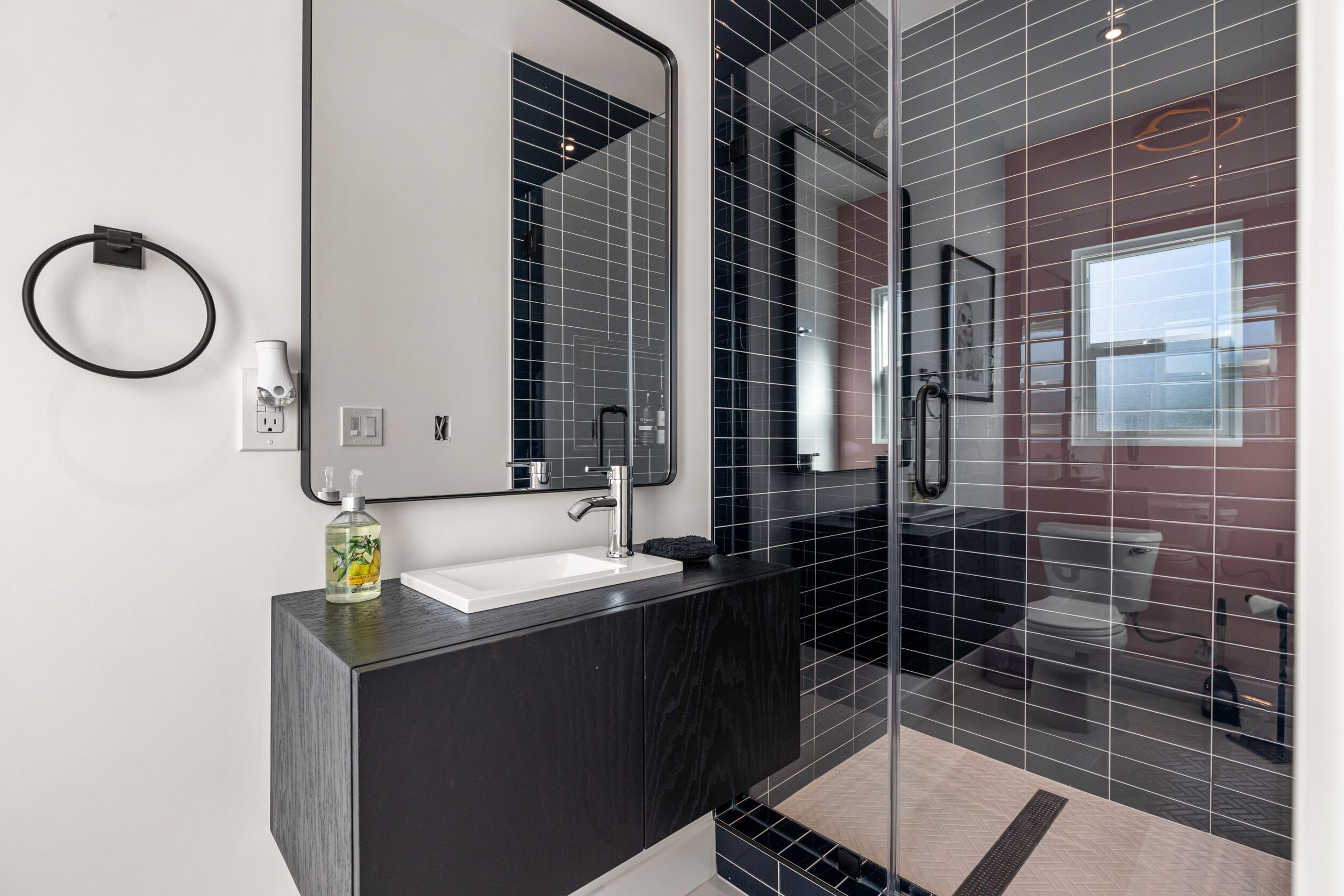 A modern bathroom with a glass-enclosed shower, a white sink, and a black countertop.