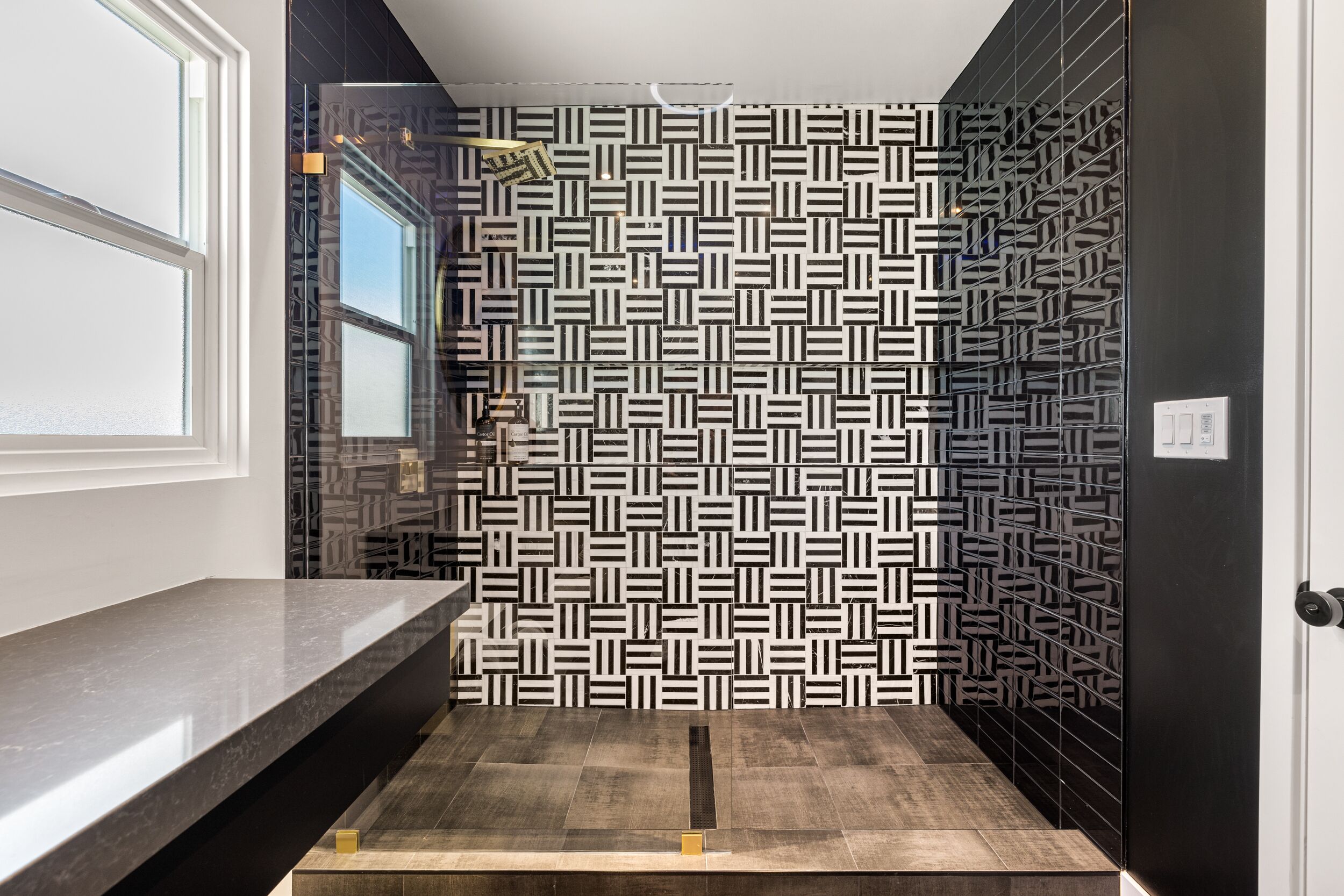 Ein modernes Badezimmer mit einer Wand in geometrischem Muster, einer dunklen Arbeitsplatte und einem sichtbaren Duschbereich.